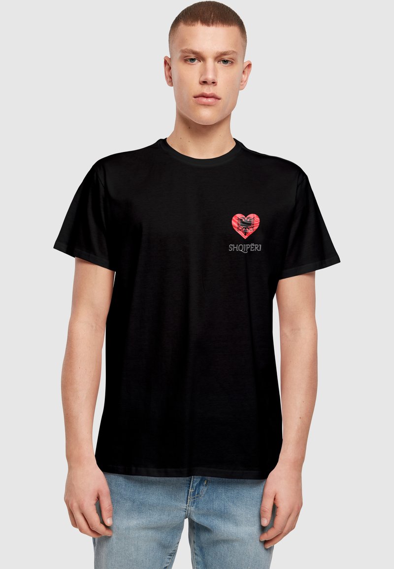 Black cotton t-shirt featuring a red heart graphic with a black eagle design and the word "SHQIPËRI" underneath. Straight-cut design.