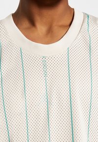 Gros plan d'une personne portant un t-shirt en mesh blanc à rayures verticales bleu sarcelle et à col rond.