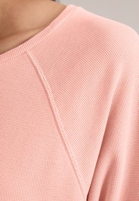 Heller rosa strukturierter Pullover mit einem gerippten Muster. Verfügt über einen weiten Ausschnitt und Raglanärmel, die einen weichen, gewebten Stoff betonen.