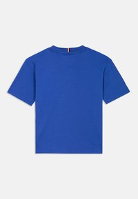 T-shirt de algodão azul com mangas curtas, decote redondo e um pequeno detalhe vermelho, branco e azul na parte de trás do decote. Design simples, sem padrões.