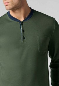 Maglietta a maniche lunghe verde scuro con colletto blu navy, tre bottoni e una piccola tasca sul petto. Tessuto liscio e design aderente.