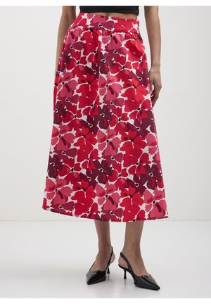 Vrouw draagt een hoge taille A-lijn midi-rok met een rood en roze bloemenpatroon en zwarte slingback hakken met puntige neus.