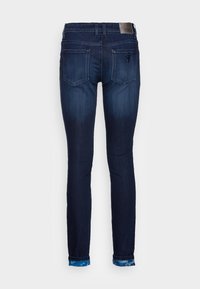 Jeans skinny de mezclilla azul oscuro con un lavado ligeramente descolorido, cinco bolsillos y puños doblados con un acento de tie-dye azul claro.