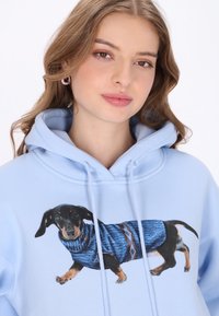 Világoskék kapucnis pulóver nyomtatott tacskóval, kék mintás pulóverben. Puha anyag, húzózsinóros kapucnival és kenguruzsebbel.