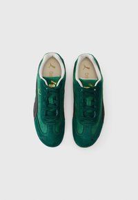 Green suede Puma sneakers with black accents and gold logos, shown from above on a plain white background.