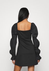 Černé mini šaty se čtvercovým výstřihem na zádech, s nabíranými rukávy a hladkým, elastickým materiálem. Jednoduchý a přiléhavý design.