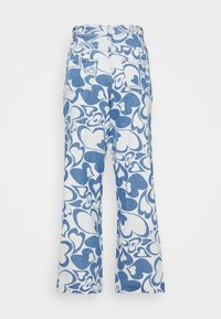 Calças de ganga em estilo boca de sino com um padrão de corações azuis sobre um fundo branco. Apresentam uma cintura alta e bolsos traseiros.