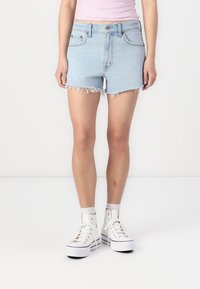 Lys blå denimshorts med frayed kant, med fem lommer og beltehemper, sammen med hvite høye sneakers.