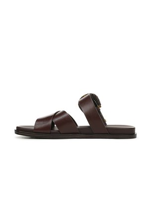 Bruine leren sandalen met kruisriemen, platte zool en een decoratief accent aan de achterkant. Gladde textuur en minimalistisch ontwerp.