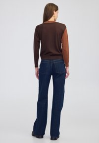 Bruine en roestkleurige trui met lange mouwen, gecombineerd met donkerblauwe wijde jeans. Gladde textuur; eenvoudig ontwerp met een detail aan de achterkant.