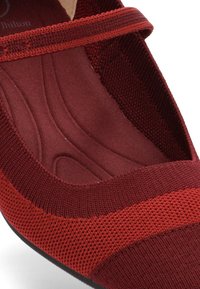 Zapato de punto rojo con una amplia correa, interior acolchado y suela lisa. Parte superior texturizada con acentos en contraste y diseño sin costuras.