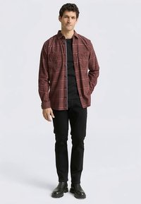 Rood geruit overhemd met twee borstzakken, gedragen over een zwart T-shirt, gecombineerd met zwarte broek en zwarte enkellaarzen.