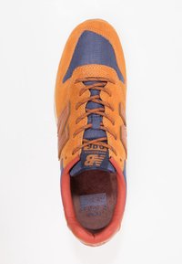 Oranžové semišové tenisky s námořnickými textilními panely, kulatými tkaničkami a polstrovaným červeným límcem. Obsahují logo a polstrovanou stélku.