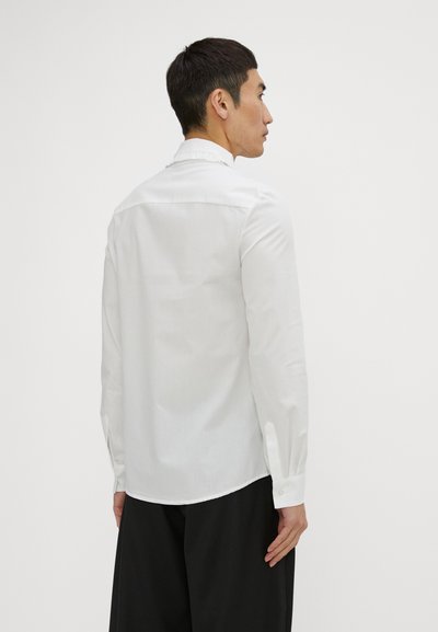 White long-sleeve shirt with a button-down collar, smooth fabric, and a curved hem, featuring buttoned cuffs and a subtle ribbed texture.