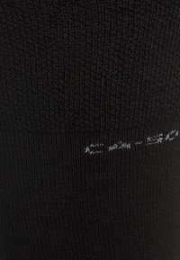 Black sock featuring a ribbed texture with a smooth finish. Contains white printed text near the top.