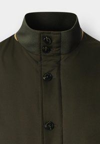 Olijfgroene jas met een hoge kraag, met een gladde textuur, vier zwarte knopen en contrasterende kleuraccenten bij de kraagnaad.