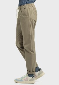 Beige, elastische Hose mit Gummibund und Kordelzug, Taschen an den Seiten, schmal zulaufendem Bein und einer glatten Textur. Kombiniert mit leichten, mehrfarbigen Sneakern.