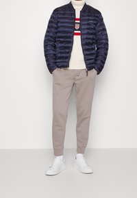 Giacca puffer blu navy, maglione cremoso a coste con strisce rosse/blu, pantaloni felpa grigi chiari e sneakers bianche. Design minimalista e vestibilità rilassata.