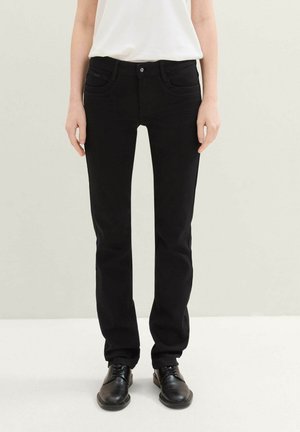 Čierne denimové nohavice so slim fit strihom; obsahujú predné vrecká, zapínanie na gombík a jemné detaily prešívania. Skombinované s čiernymi topánkami a bielym topom.