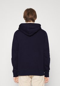 Navy blue hoodie with a kangaroo pocket, ribbed cuffs, and hem. Fabric appears smooth with a relaxed fit and a drawstring hood.