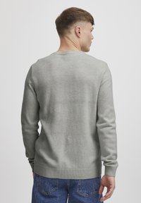 Pull léger gris en maille douce avec un col rond et des poignets et un ourlet côtelés, vu de l'arrière.