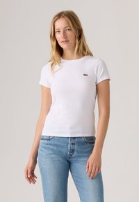 T-shirt branca de algodão com mangas curtas e decote redondo, apresentando um pequeno logótipo vermelho da Levi's no peito esquerdo. Ajuste casual e design sem costuras.