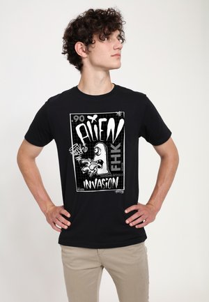 T-shirt di cotone nero con una grafica bianca che presenta il testo "ALIEN INVASION" e un alieno in stile cartoon con un'espressione esagerata.