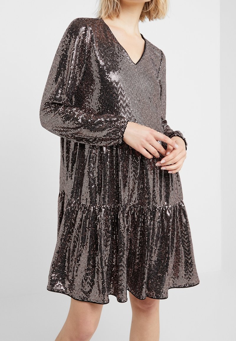 Robe pailletée avec un décolleté en V, des manches longues et une jupe à volants. Présente un motif métallique rose doré et une texture douce.