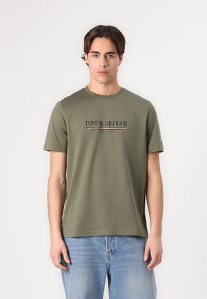 Olivgrünes Baumwoll-T-Shirt mit Rundhalsausschnitt und kurzen Ärmeln, mit dem kontrastierend bedruckten "TOMMY HILFIGER"-Logo auf der Vorderseite.