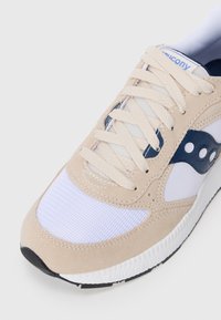 Beige sneaker featuring a combination of suede and mesh materials, with white and navy accents, thick white sole, and textured surface.
