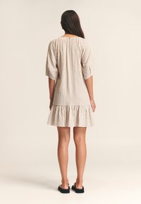 Abito a righe con maniche a tre quarti, scollatura arricciata, orlo ondulato, in beige e marrone chiaro, realizzato in tessuto leggero.