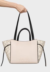 Bolso tote rosa y beige con acentos negros, que presenta una textura suave y un logotipo en relieve. Patrón único en los laterales. Largos asas negras.