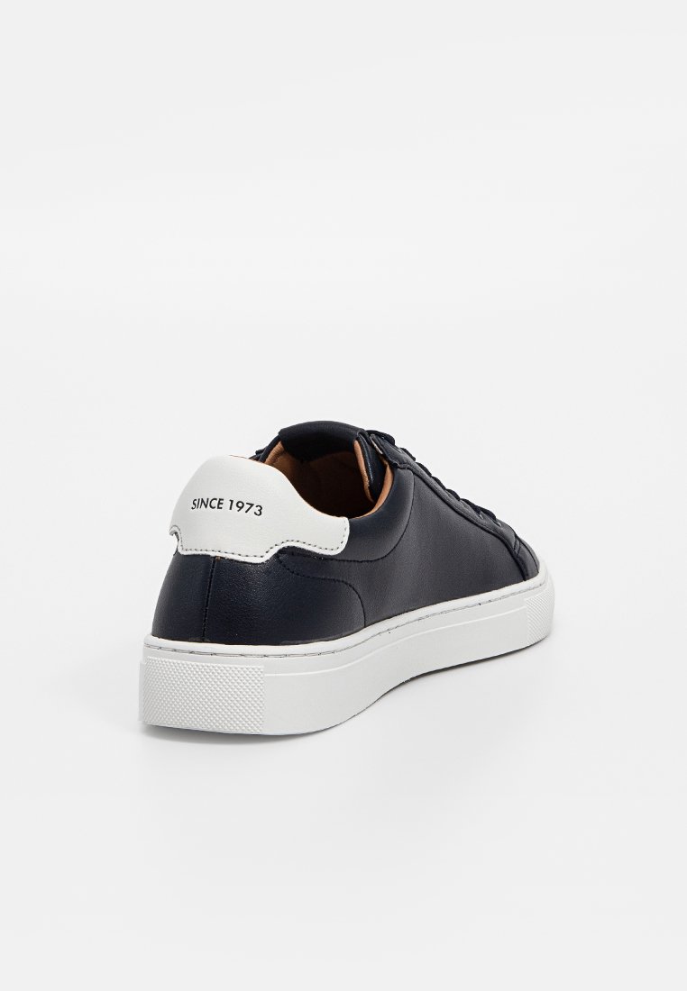 Czarna skórzana sneaker z białą naszywką na pięcie oznaczoną "SINCE 1973", biała gumowa podeszwa i czarne sznurowadła na białym tle.