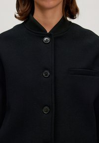 Zwarte wollen mix knoop-jas met een geribbelde kraag, voorzien van vijf knopen en een enkele borstzak. Houdt een gladde textuur en een minimalistisch ontwerp.