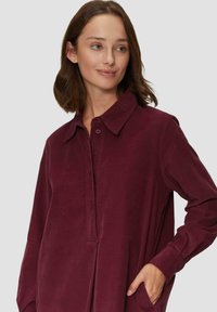 Burgunderfarbenes Langarmhemd mit Kragen und Button-Down-Front, mit lockerem Schnitt und Seitentaschen. Weiche Textur.