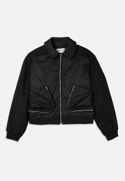 Black bomber jacket with a zip front, fabric contrasting sleeves, and two large zippered pockets on the front. Smooth, shiny texture.