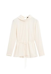 Blouse crème à manches longues avec un col haut et une taille cintrée. Présente un lien à la taille et un tissu lisse et texturé.