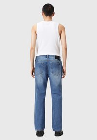 Niebieskie dżinsy z luźnym krojem, z dwoma tylnymi kieszeniami i czarną metką na wysokości pasa. Noszone z białym topem na ramiączkach.
