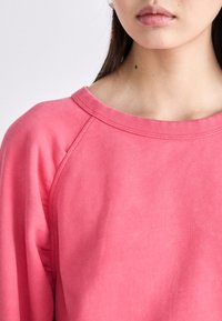 Sudadera rosa con cuello redondo acanalado y mangas raglán, con un tejido suave y texturizado y un corte holgado.
