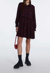 Schwarz und dunkelrosa tigerstreifenkleid mit langen Ärmeln, Knopfleiste, schichtweisem Design, kombiniert mit schwarzen Knöchelstiefeln und einer roten Umhängetasche.