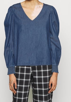 Denim-Oberteil mit V-Ausschnitt, langen Puffärmeln und gerafften Bündchen. In einem mittelblauen Farbton und mit lässiger Passform. Kombiniert mit karierten Hosen.