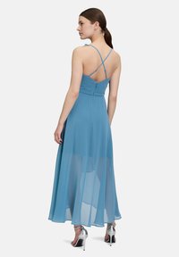 Ein langes, fließendes blaues Kleid mit enganliegender Taille und gekreuzten Trägern im Rücken; durchscheinender Stoff reicht bis zu einem mehrlagigen Rock.