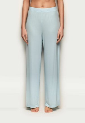 Frau steht barfuß und trägt hellblaue, locker sitzende, weit geschnittene Hosen mit elastischem Bund.