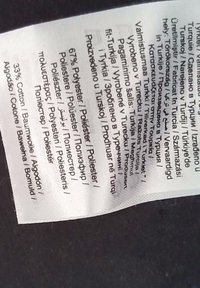 Étiquette indiquant la composition du tissu : 67 % polyester, 33 % coton. Comprend plusieurs langues avec les instructions d'entretien sur une étiquette en tissu blanche.