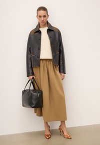 Czarna skórzana kurtka zapinana na guziki, beżowy sweter dzianinowy, brązowa spódnica plisowana, czarna torebka i brązowe szpilki w kropki.