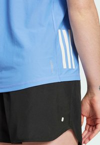 Lichtblauw sportshirt met een gestructureerde afwerking, voorzien van drie witte strepen aan de zijkant. Zwarte shorts met een afgeronde zoom en een klein logo detail.