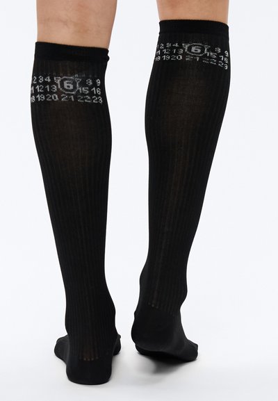 Mustad põlveni ulatuvad sokid vertikaalse sooniku ja numbrilise mustriga kontrastvalges, ühevärvilise ning õmblusteta varbaga.