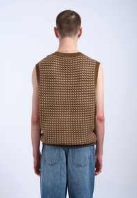 Bruin gebreid mouwloos vest met een gestructureerd patroon, met een ribnek en -zoom, gecombineerd met vervaagde blauwe jeans.