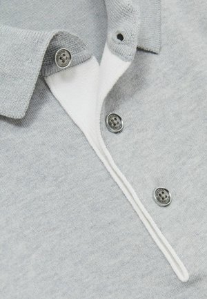 Polo gris clair avec un col blanc, comportant trois boutons en métal argenté et un tissu doux et texturé. Couture accentuée le long de l'ouverture.