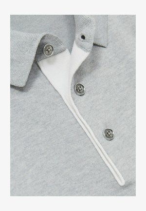 Svetlo siva polo majica z belim ovratnikom, opremljena s tremi srebrnimi gumbi in mehkim, teksturiranim materialom. Okrasek z nitmi vzdolž tlačnega šiva.